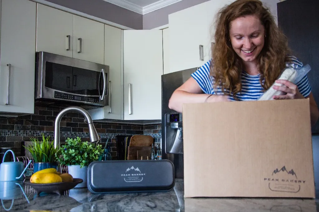 A happy customer unboxing a frozen delivery box on her kitchen counter