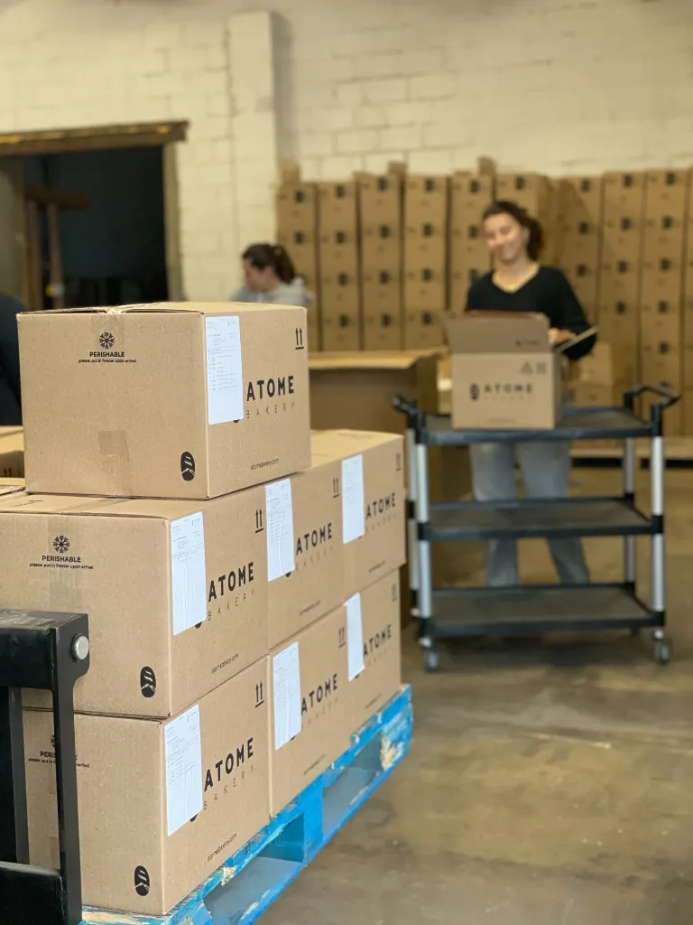 Atome Bakery boxes stacked on a pallet while the team packs orders in the F2C Vancouver warehouse